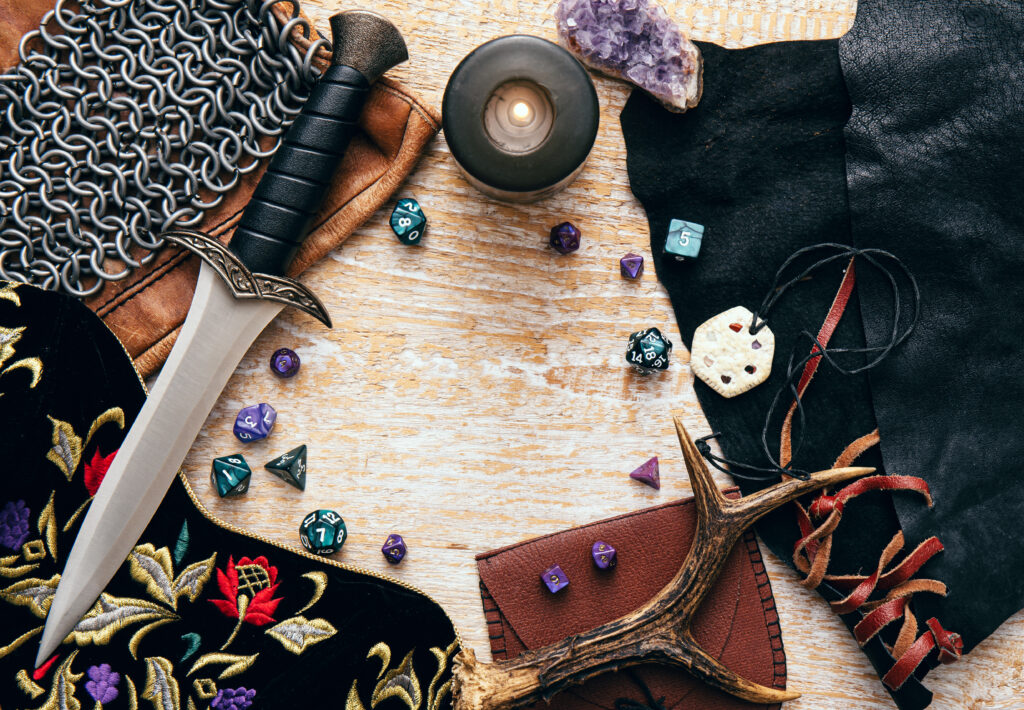 A dagger, some dice and other TTRPG stuff on a wooden table.